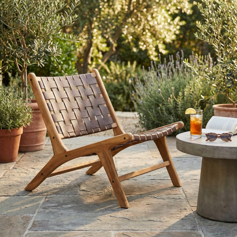 Poltrona lounge Alexander in teak massello posizionata su un patio in pietra accanto a un tavolino in cemento.