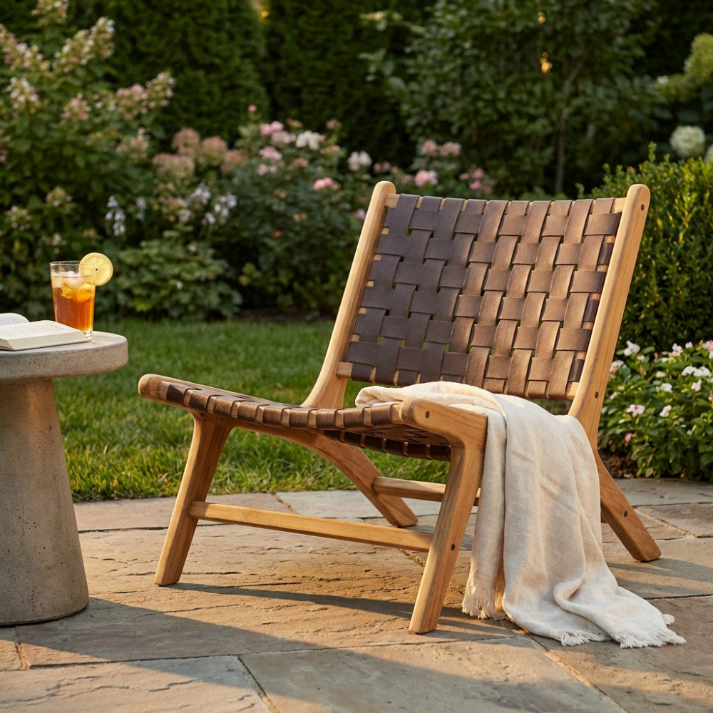 Vista laterale della poltrona in teak Alexander con una coperta in lino drappeggiata in un giardino rigoglioso.