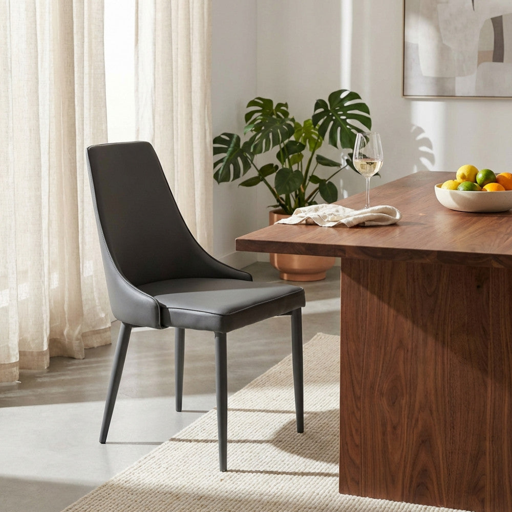 Sedia Camille in ecopelle grigio scuro posizionata accanto a un tavolo da pranzo in legno massello in un ambiente moderno.