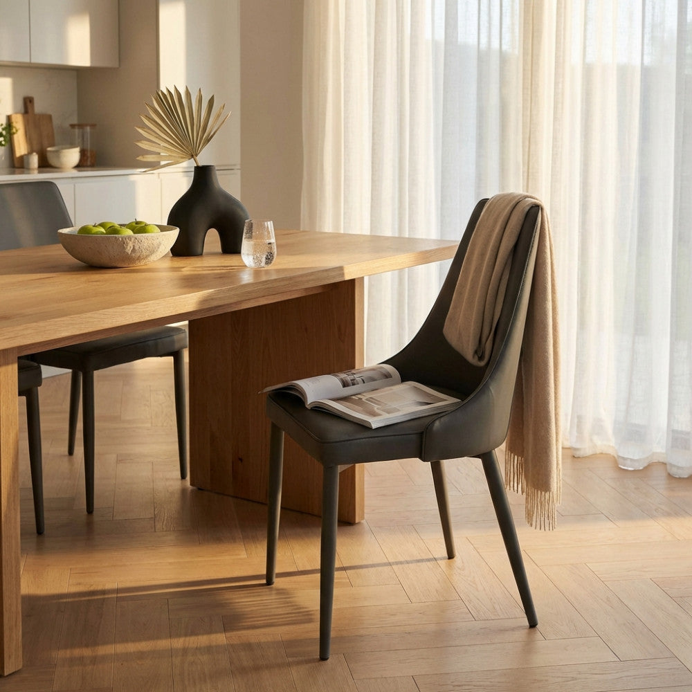 Sedia Camille grigio chiaro con un plaid beige appoggiato, accanto a un tavolo in rovere.