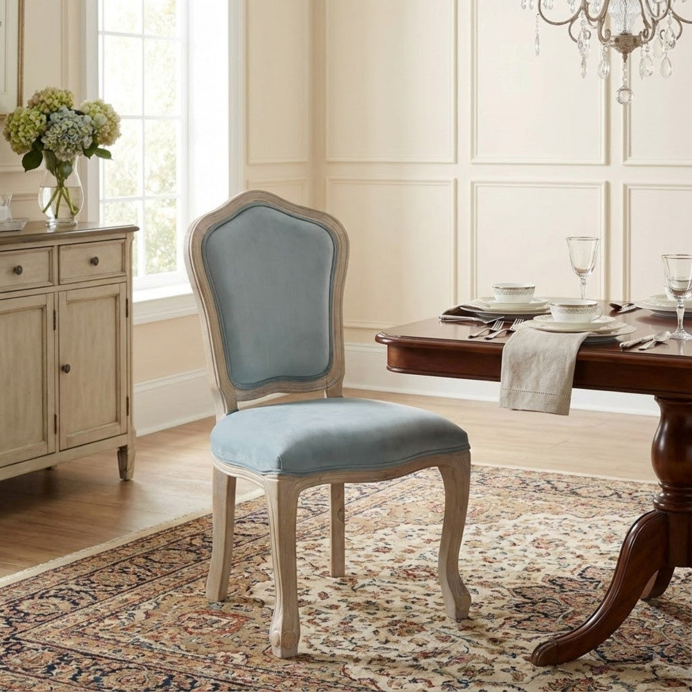 Sedia Charlene in velluto grigio ambientata in una sala da pranzo classica con tappeto decorativo.