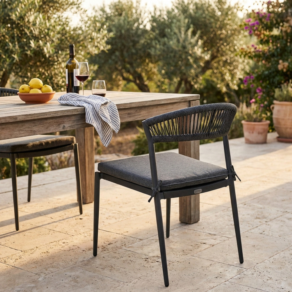 Vista posteriore della sedia Corrientes accanto a un tavolo da pranzo in un rigoglioso giardino mediterraneo.