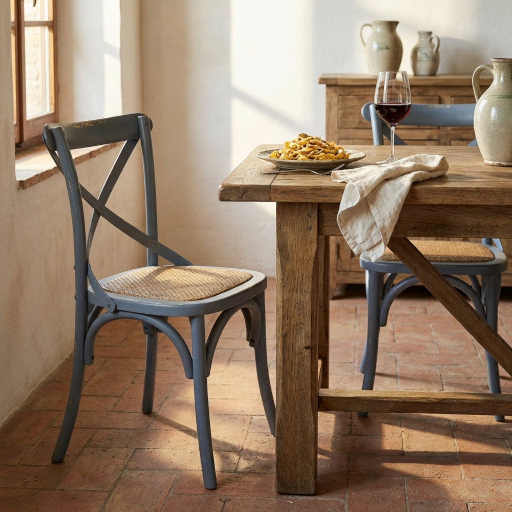 Sedia Cross Grigia in legno posizionata accanto a un tavolo rustico imbandito in una sala da pranzo luminosa.