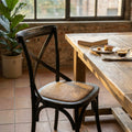 Sedia rustica Cross Nero in legno e rattan ambientata in una sala da pranzo luminosa.