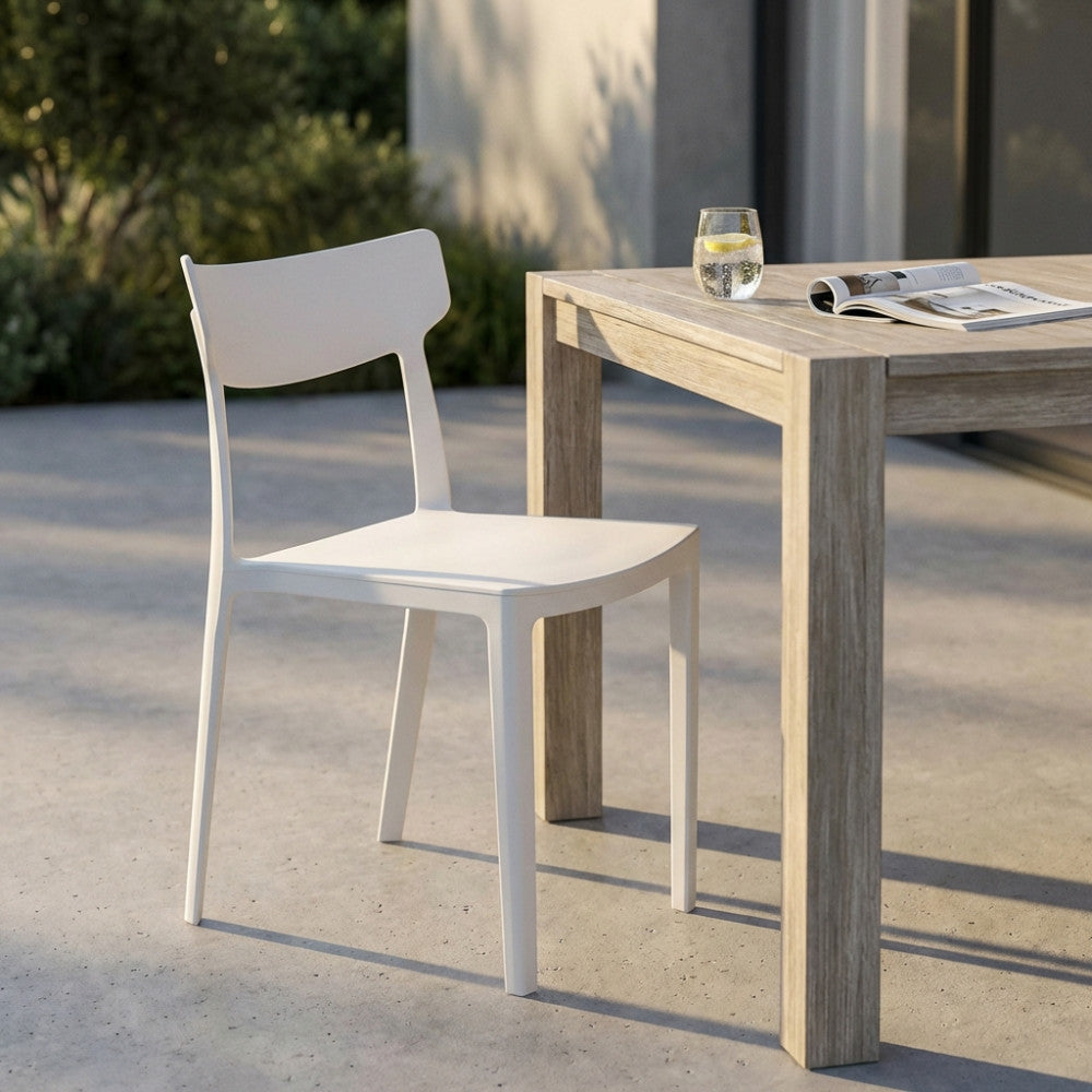 Sedia bianca di design senza braccioli su una terrazza in cemento, abbinata a un tavolo in legno chiaro illuminato dalla luce solare.