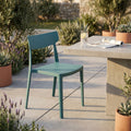 Sedia in polipropilene blu Debby ambientata all'aperto su un patio in cemento, accanto a un tavolo moderno e piante mediterranee.