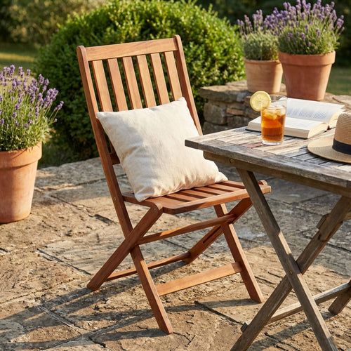 Sedia pieghevole Diana in legno di acacia marrone, ambientata in un giardino soleggiato accanto a un tavolo in legno e vasi di lavanda.