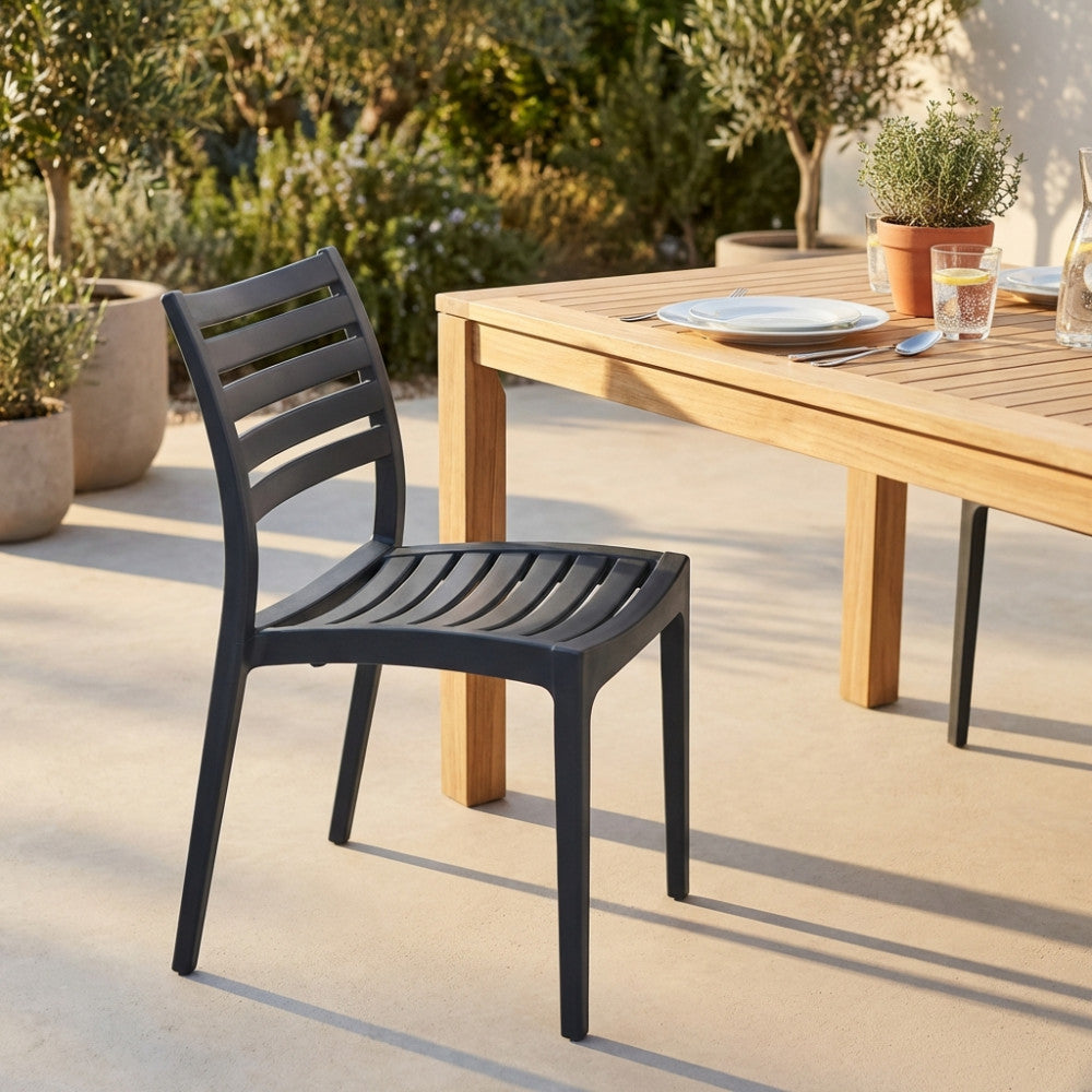 Sedia da esterno Eveline color antracite posizionata accanto a un tavolo in legno di teak in un giardino soleggiato.