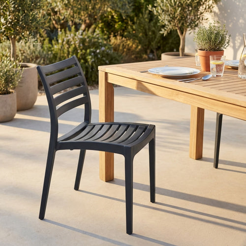 Sedia da esterno Eveline color antracite posizionata accanto a un tavolo in legno di teak in un giardino soleggiato.