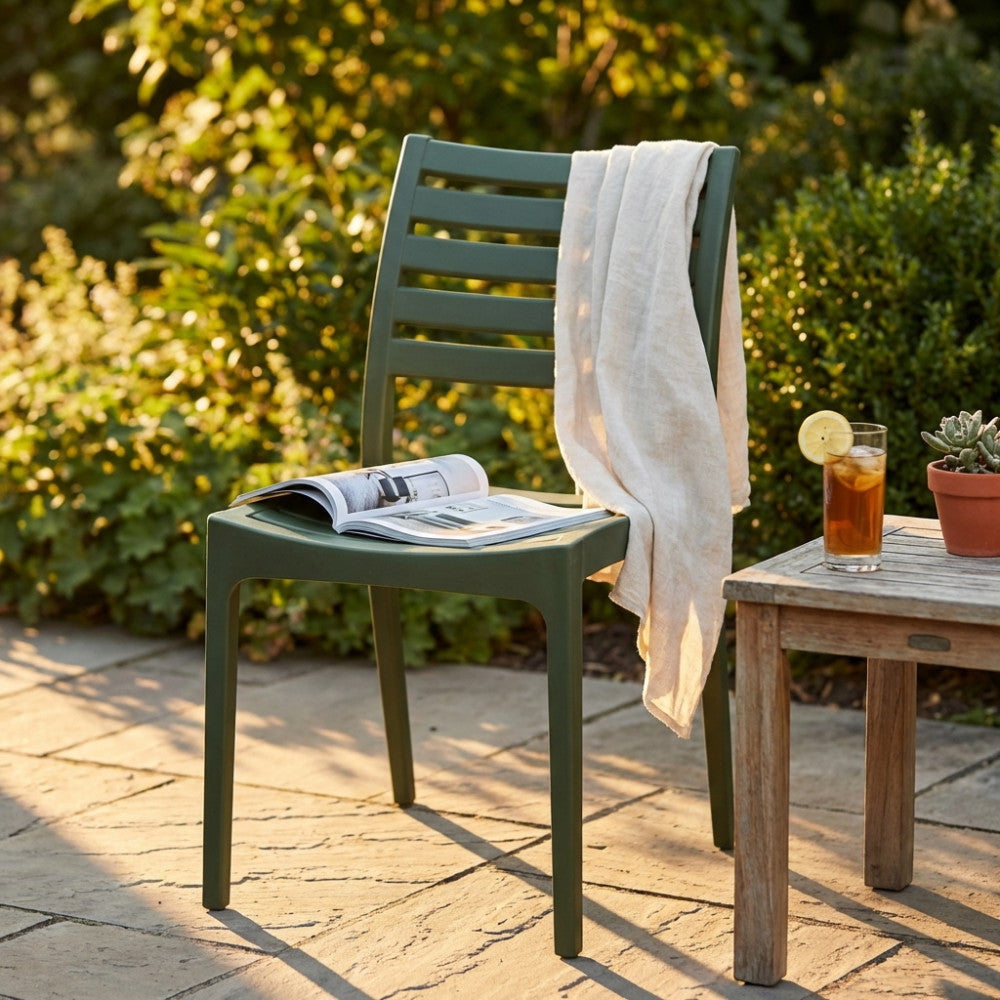 Sedia Eveline verde oliva ambientata in un giardino al tramonto, accostata a un tavolino in legno e un telo in lino.