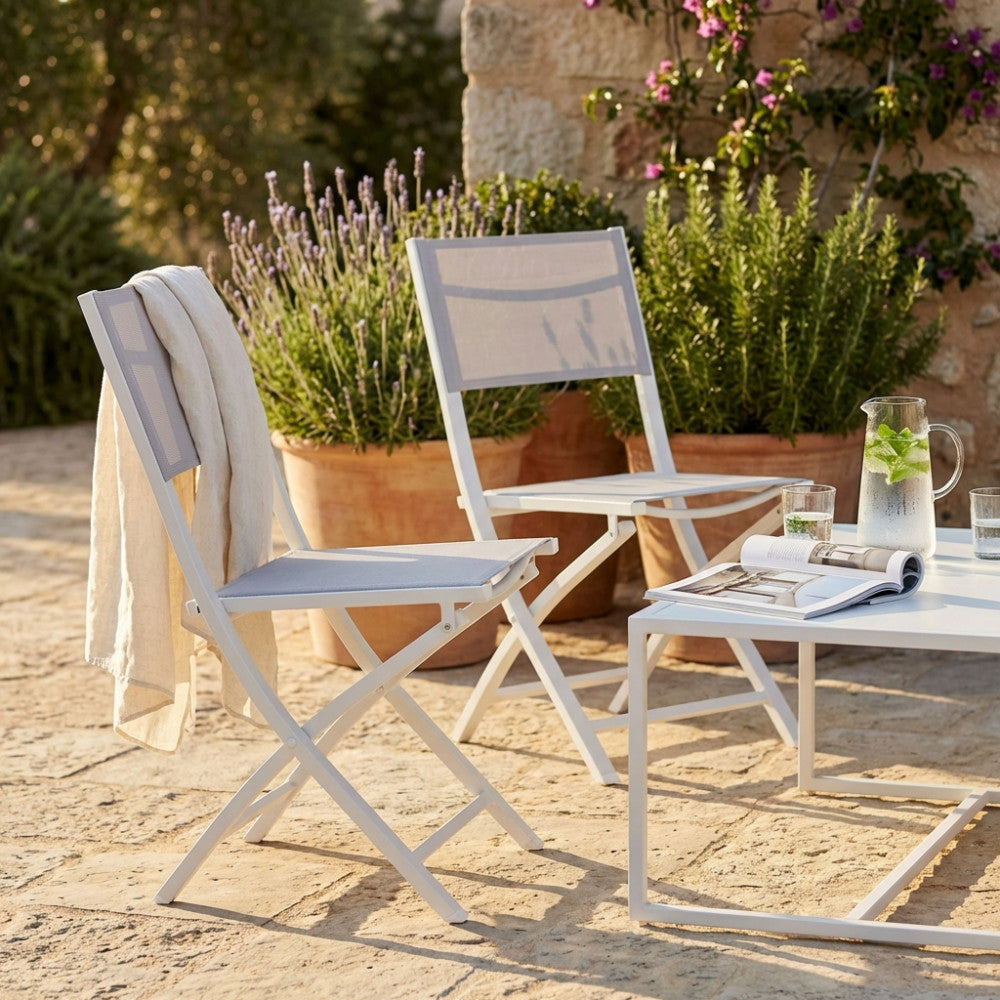 Sedia pieghevole Georgia in alluminio bianco e textilene grigio ambientata in un giardino rustico al tramonto.
