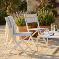 Sedia pieghevole Georgia in alluminio bianco e textilene grigio ambientata in un giardino rustico al tramonto.