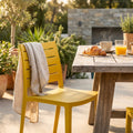 Sedia in polimero giallo Hallie posizionata all'aperto accanto a un tavolo in legno rustico con colazione.