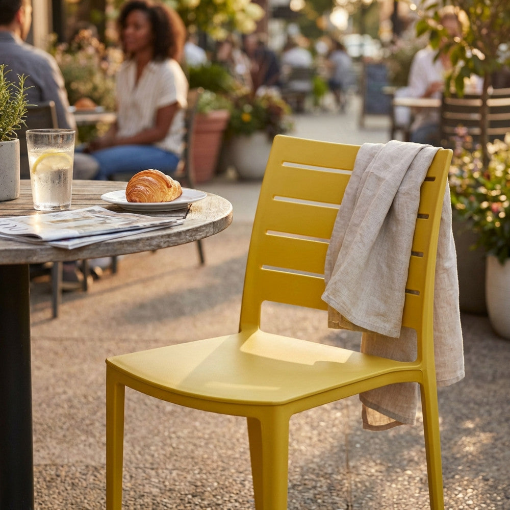 Sedia moderna gialla Hallie in un contesto di caffetteria all'aperto, illuminata dalla luce del sole.