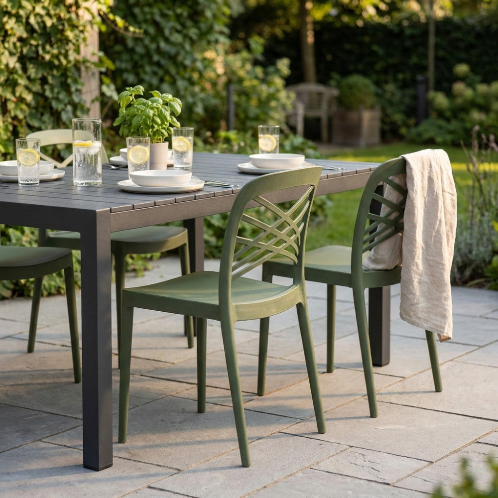 Set di sedie HARMONIE verdi attorno a un tavolo da pranzo scuro in un giardino lussureggiante.