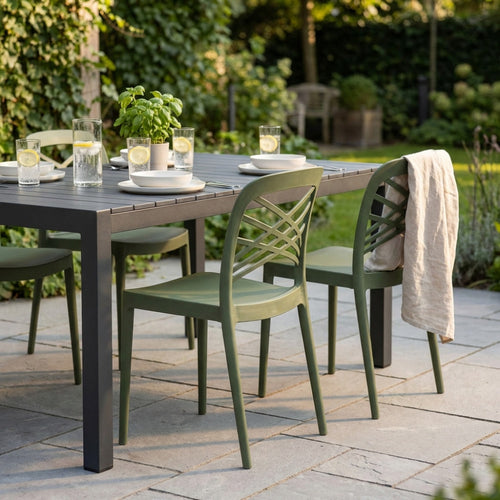 Set di sedie HARMONIE verdi attorno a un tavolo da pranzo scuro in un giardino lussureggiante.