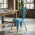 Sedia Lola in acciaio azzurro antico ambientata in un loft industriale vicino a un tavolo in legno.