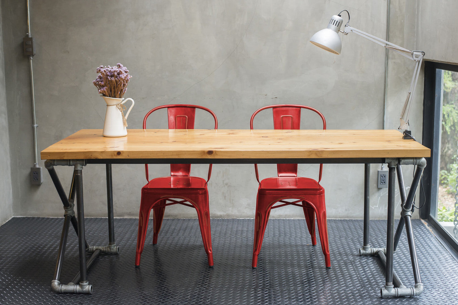 Coppia di sedie Lola Red Antico in acciaio abbinate a un tavolo in legno con gambe in tubi metallici industriali.