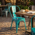 Sedia in metallo verde petrolio stile industrial ambientata all'aperto accanto a un tavolo in legno con colazione.