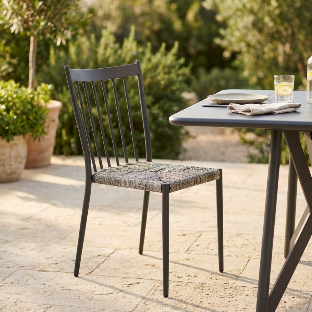Sedia Martinica in alluminio antracite e wicker ambientata all'aperto su un patio in pietra, accanto a un tavolo da pranzo.