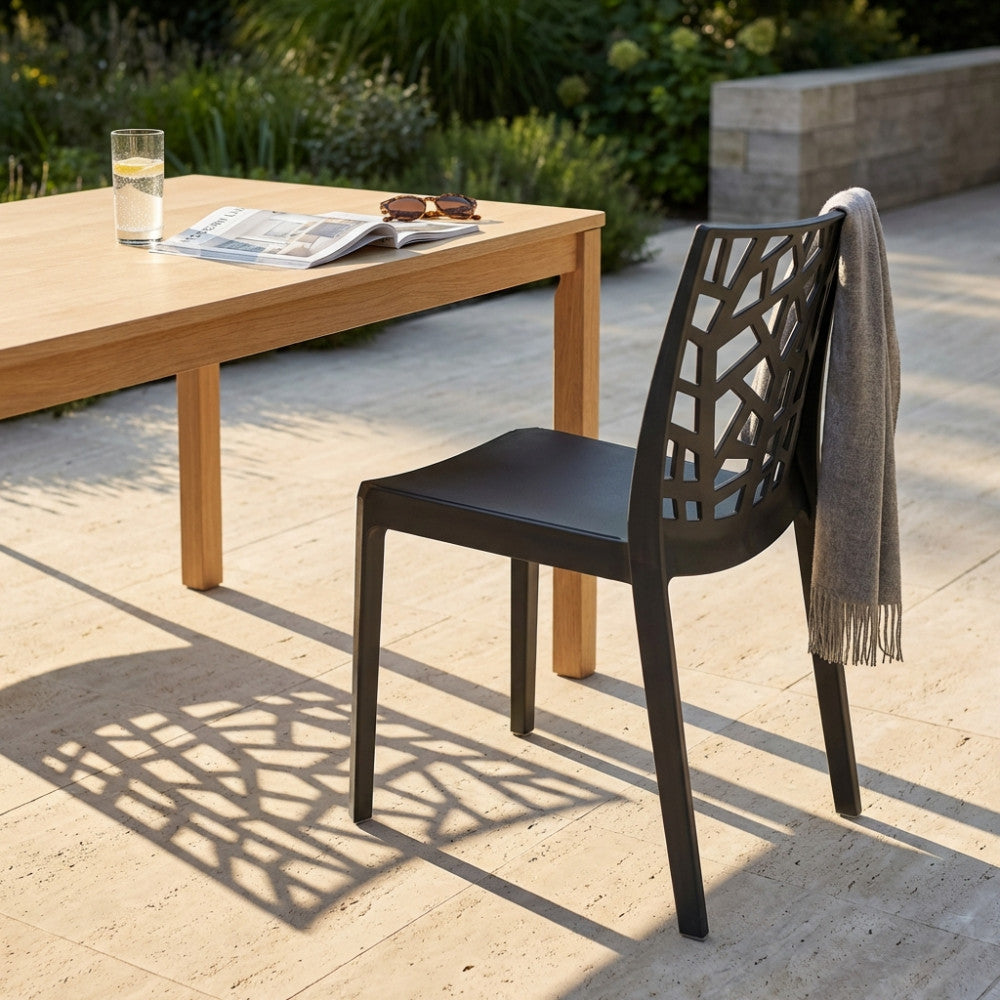 Sedia Matrix nera in polipropilene con schienale geometrico, affiancata a un tavolo in legno chiaro su un patio in pietra baciato dal sole.