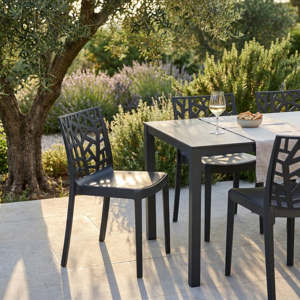 Set di sedie Matrix nere disposte attorno a un tavolo da pranzo scuro in un rigoglioso giardino mediterraneo con ulivi.