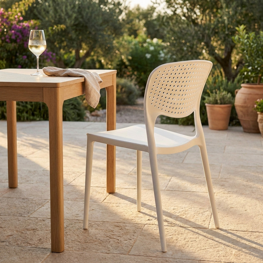 Sedia Mets in plastica bianca accostata a un tavolo in legno massello, illuminata dalla calda luce del tramonto in un patio esterno.