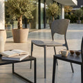 Sedia METS in plastica taupe ambientata in un patio esterno moderno con tavolino nero e tazzina da caffè.