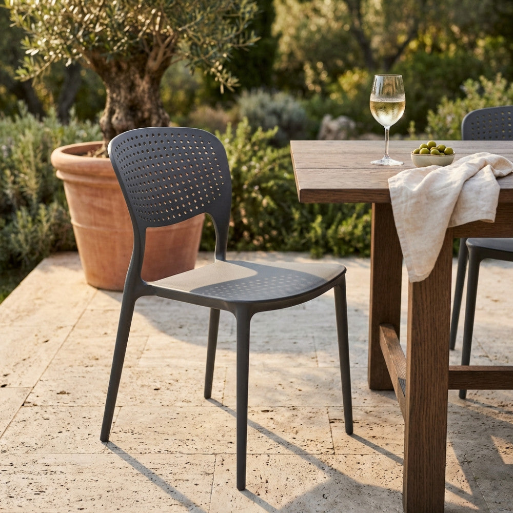 Sedia METS color taupe posizionata accanto a un tavolo in legno massello in un giardino soleggiato.