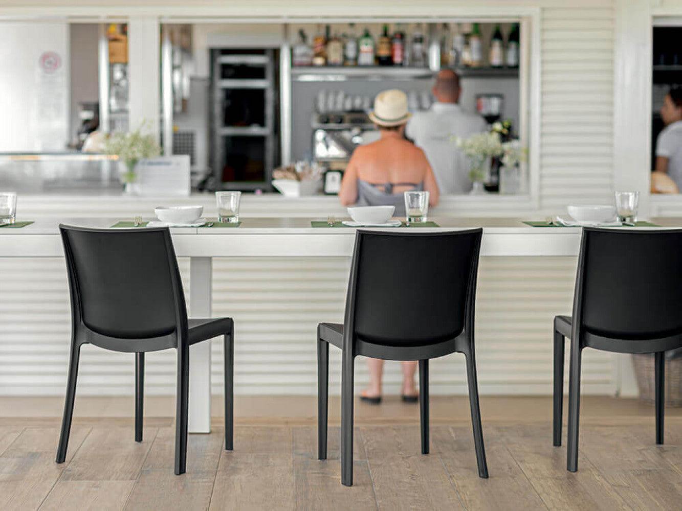 Tre sedie Perla antracite allineate al bancone di un elegante bar all'aperto.