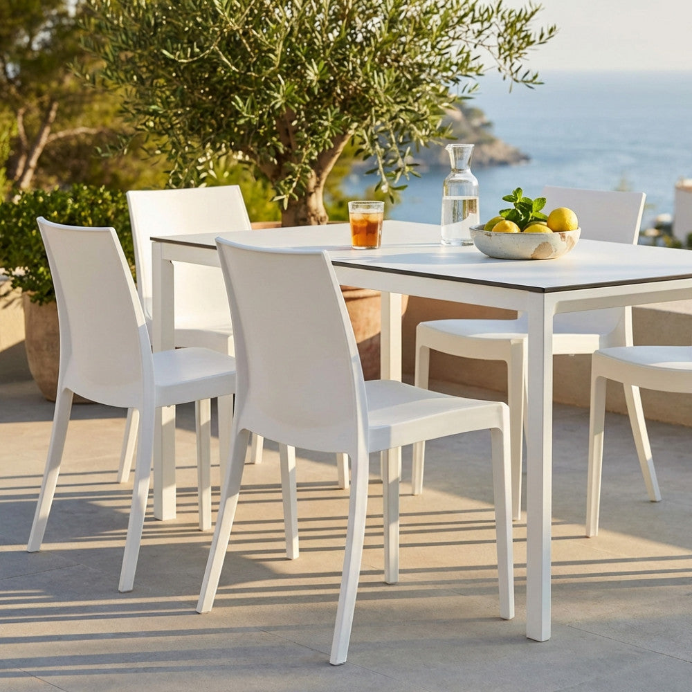 Set di sedie bianche senza braccioli disposte attorno a un tavolo da pranzo su una terrazza soleggiata.