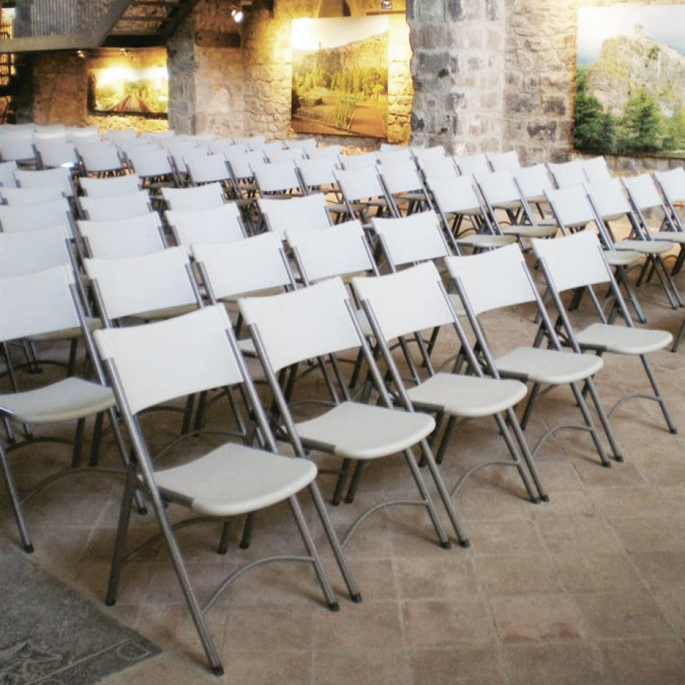 Molteplici sedie pieghevoli Catering 1 allineate ordinatamente in una suggestiva sala conferenze con pareti in pietra antica.