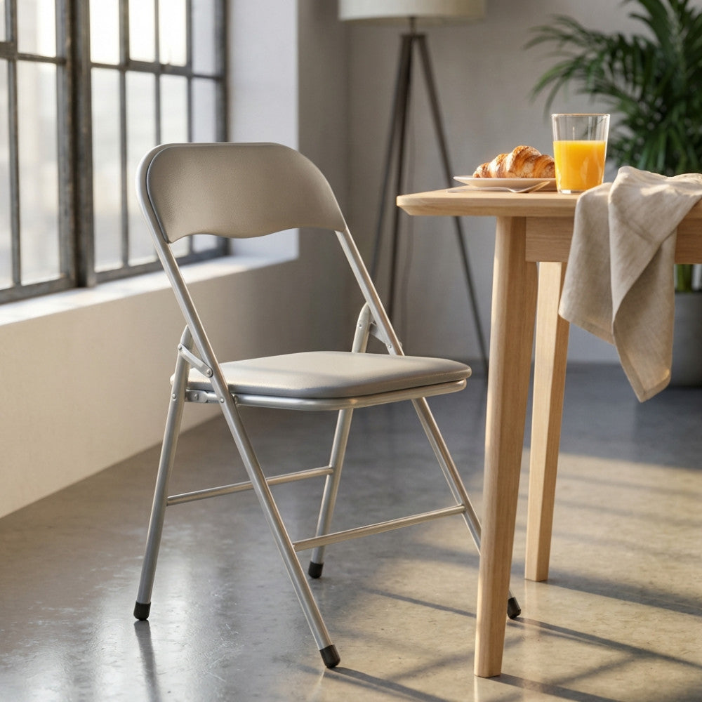 Sedia pieghevole di design grigia accostata a un tavolo da pranzo in rovere con colazione allestita, illuminata da luce naturale.