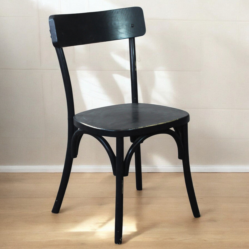 Sedia Polly nera fotografata in un ambiente minimalista con pavimento in legno chiaro e luce naturale.