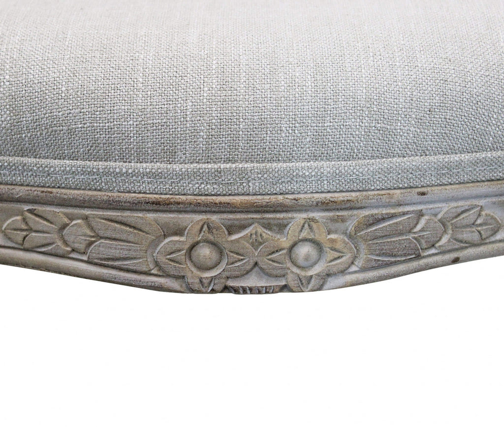 Dettaglio ravvicinato della fascia in legno intagliato con motivi floreali e del cuscino in tessuto grigio.