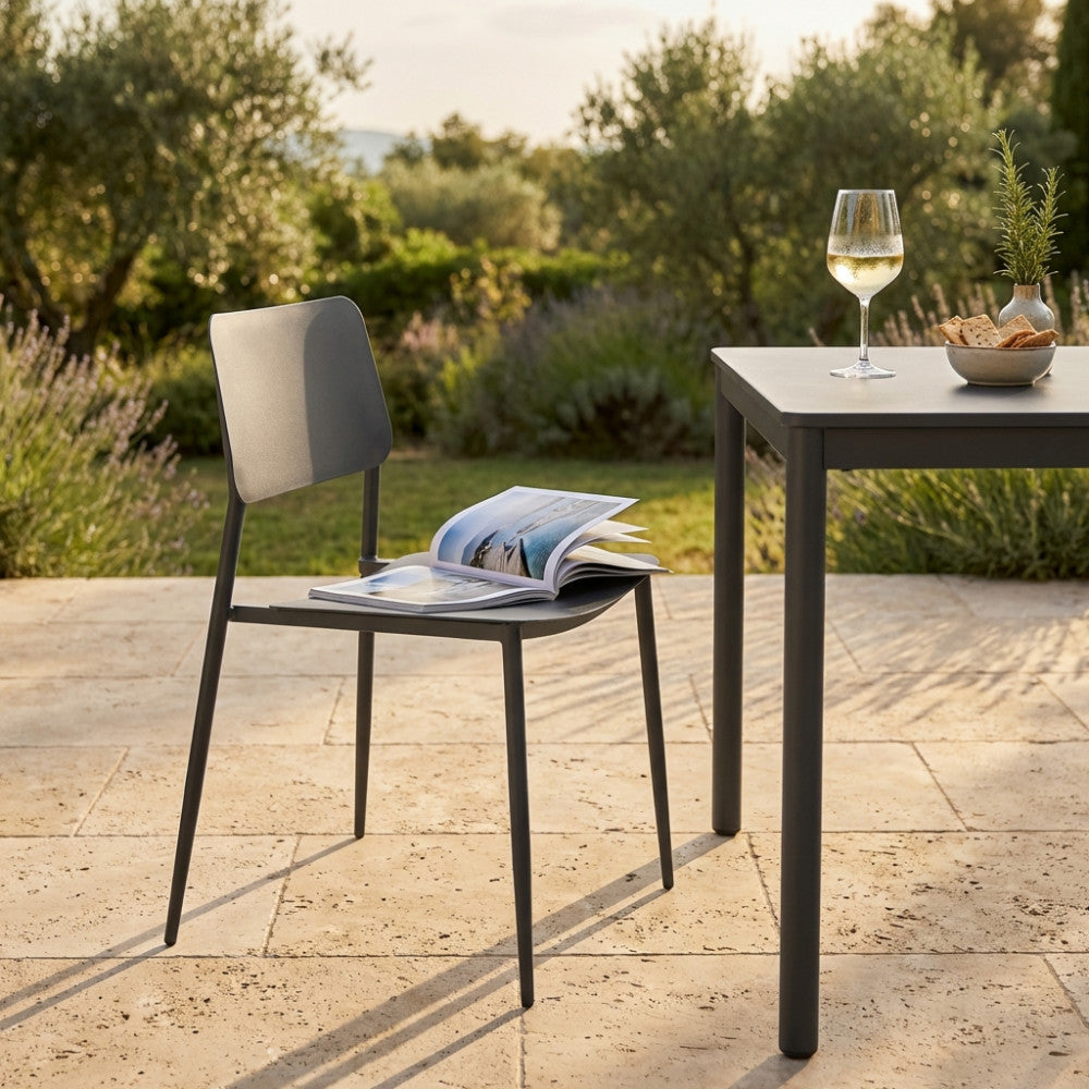 Dettaglio della sedia Vega in acciaio taupe in un contesto outdoor con una rivista appoggiata sulla seduta.