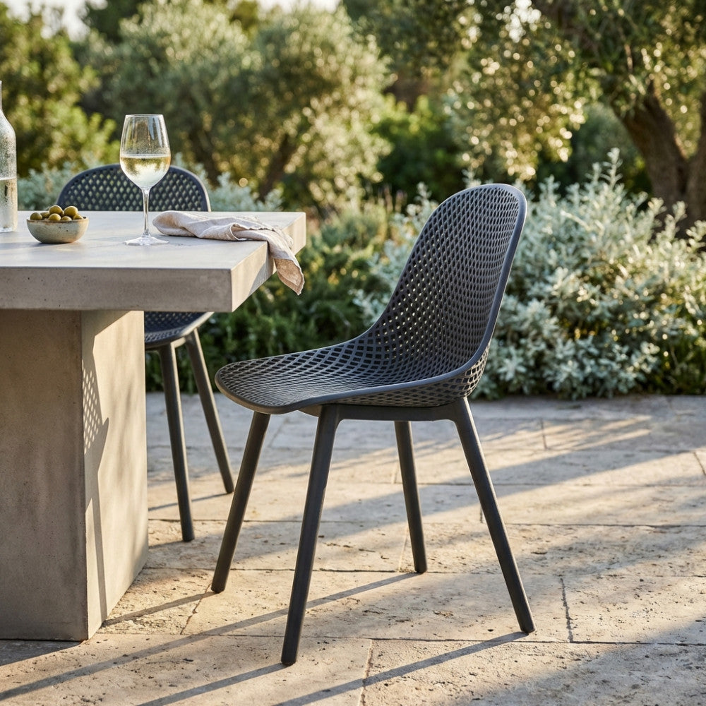 Sedia Vichy in polimero antracite illuminata dalla luce naturale su una terrazza in pietra, affiancata a un tavolo in cemento grezzo.