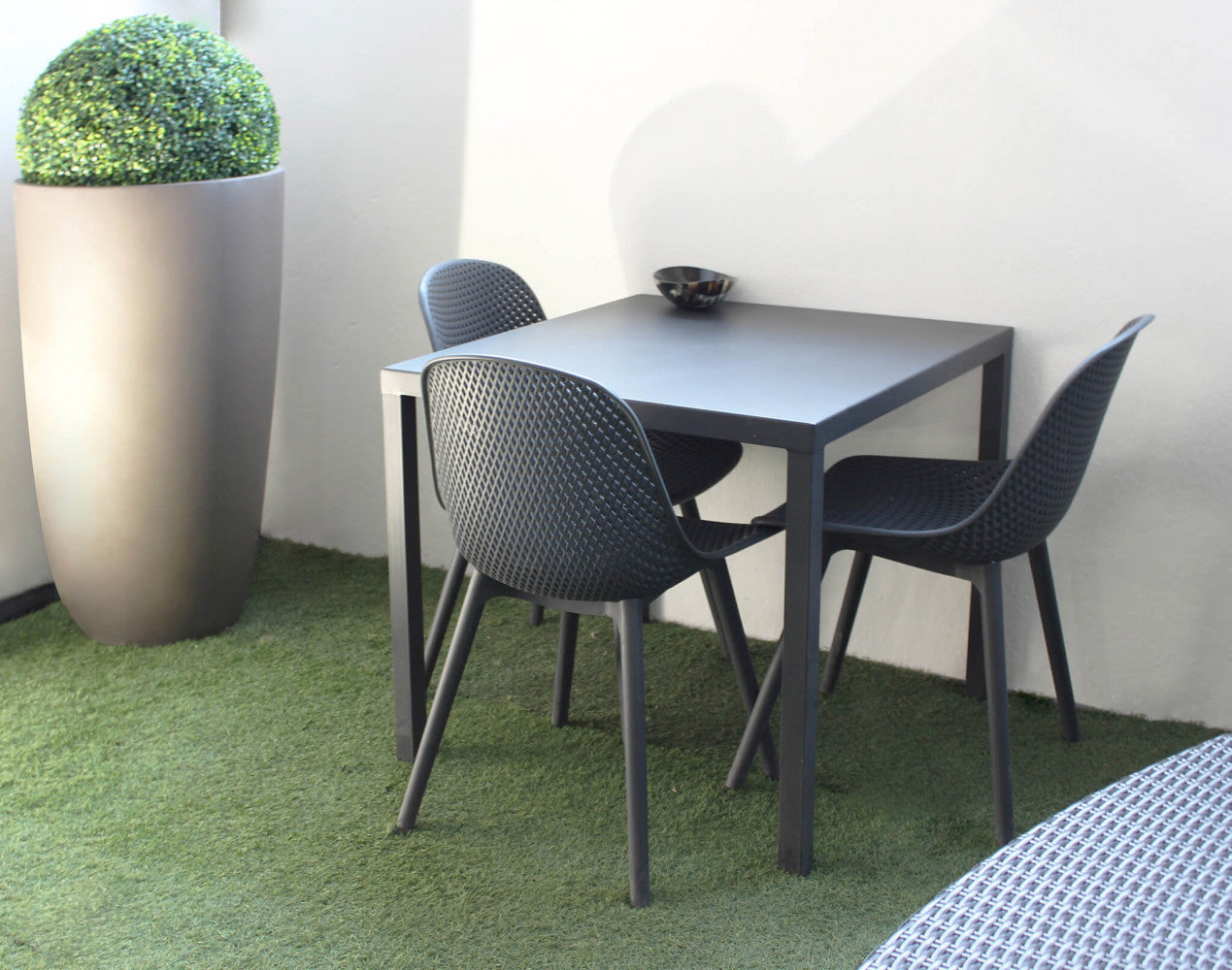 Set dining composto da tre sedie Vichy antracite e un tavolo quadrato coordinato, allestito su un prato sintetico in un ambiente outdoor contemporaneo.