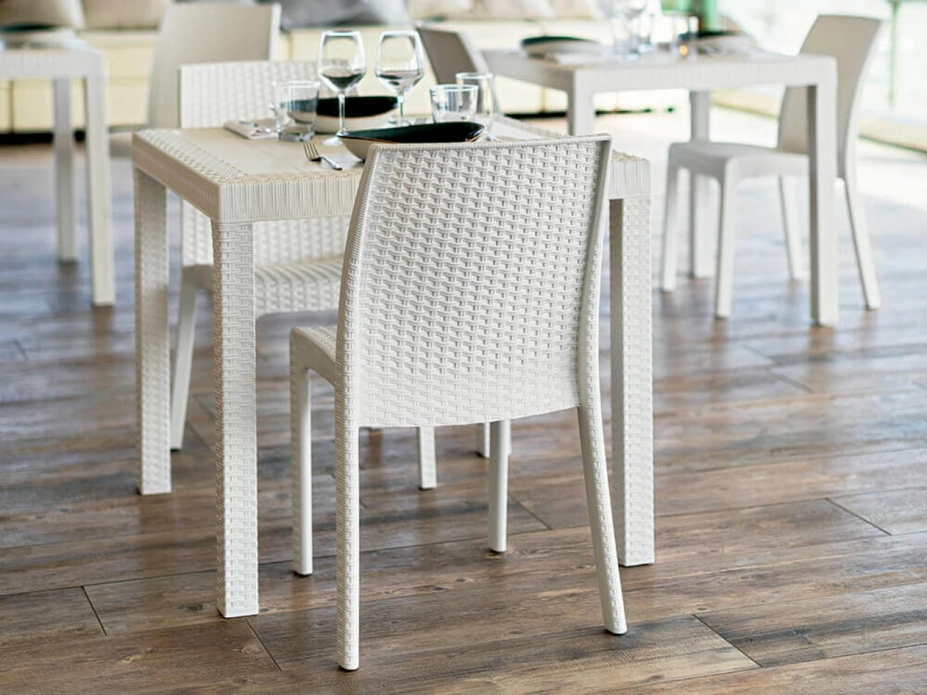 Sedia da giardino Virginia Bianca in plastica stampata effetto Wicker, design elegante resistente agli UV, ambientata in un ristorante con tavolo rettangolare