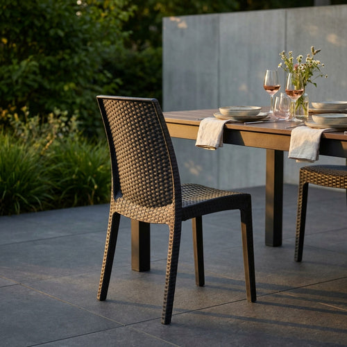 Vista di tre quarti posteriore della sedia Virginia in wicker antracite inserita in un elegante patio moderno al tramonto.