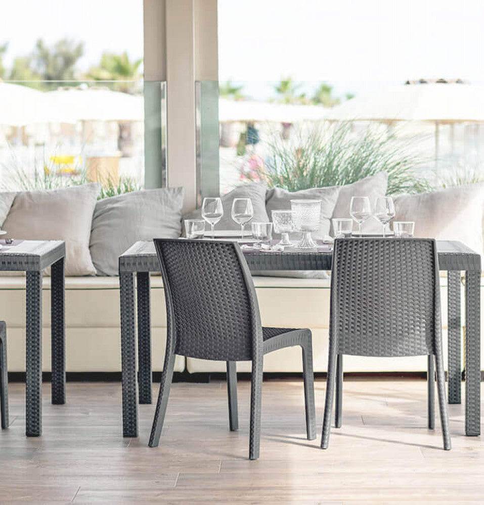 Coppia di sedie Virginia in wicker disposte in un elegante patio coperto con divani chiari e vista mare.