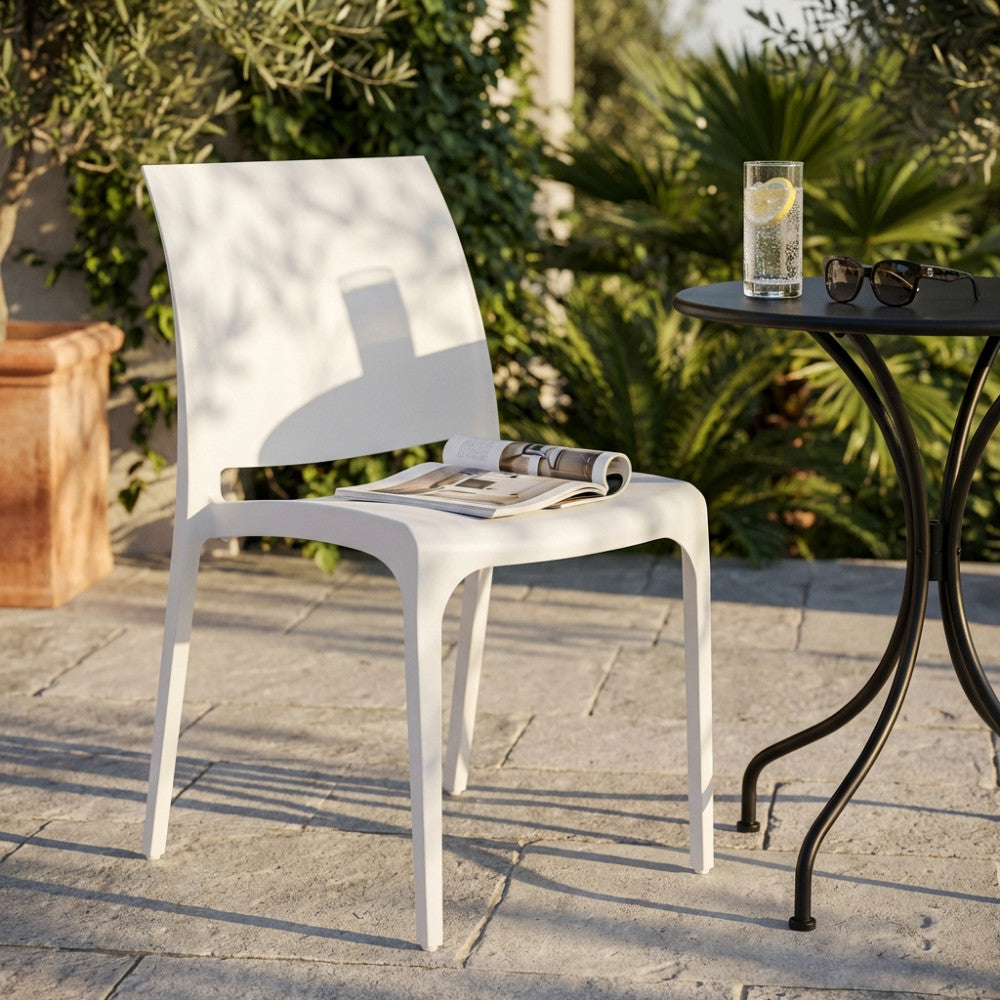Sedia Volga bianca in polipropilene posizionata su un patio in pietra accanto a un tavolino da bistrot.