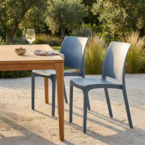 Coppia di sedie Volga blu accostate a un tavolo in legno di teak in un giardino soleggiato.