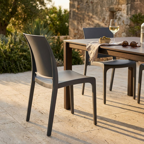 Dettaglio laterale della sedia Volga abbinata a un tavolo da pranzo all'aperto in un giardino mediterraneo.