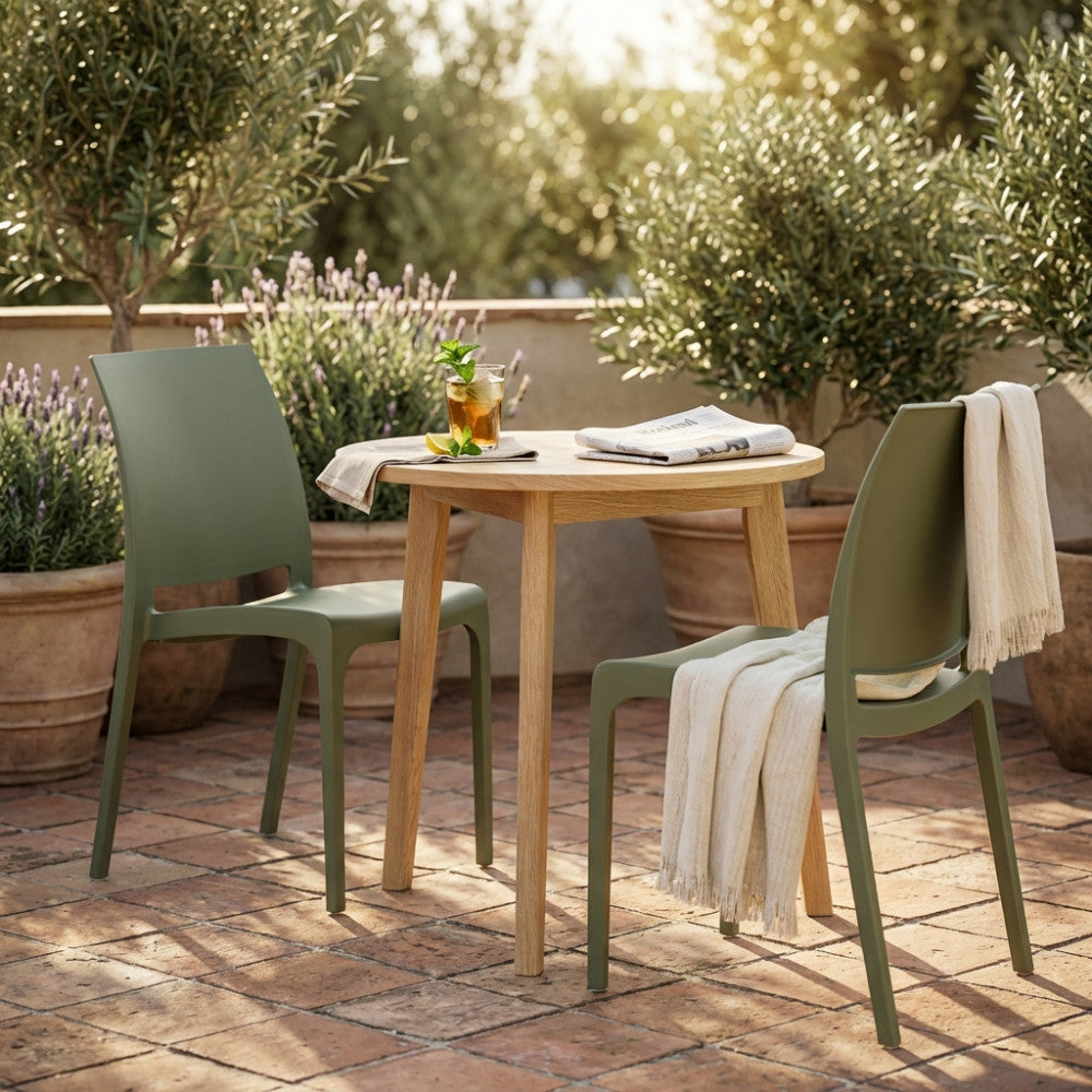 Sedia Volga verde in polipropilene abbinata a un tavolo rotondo in legno in un elegante patio esterno.