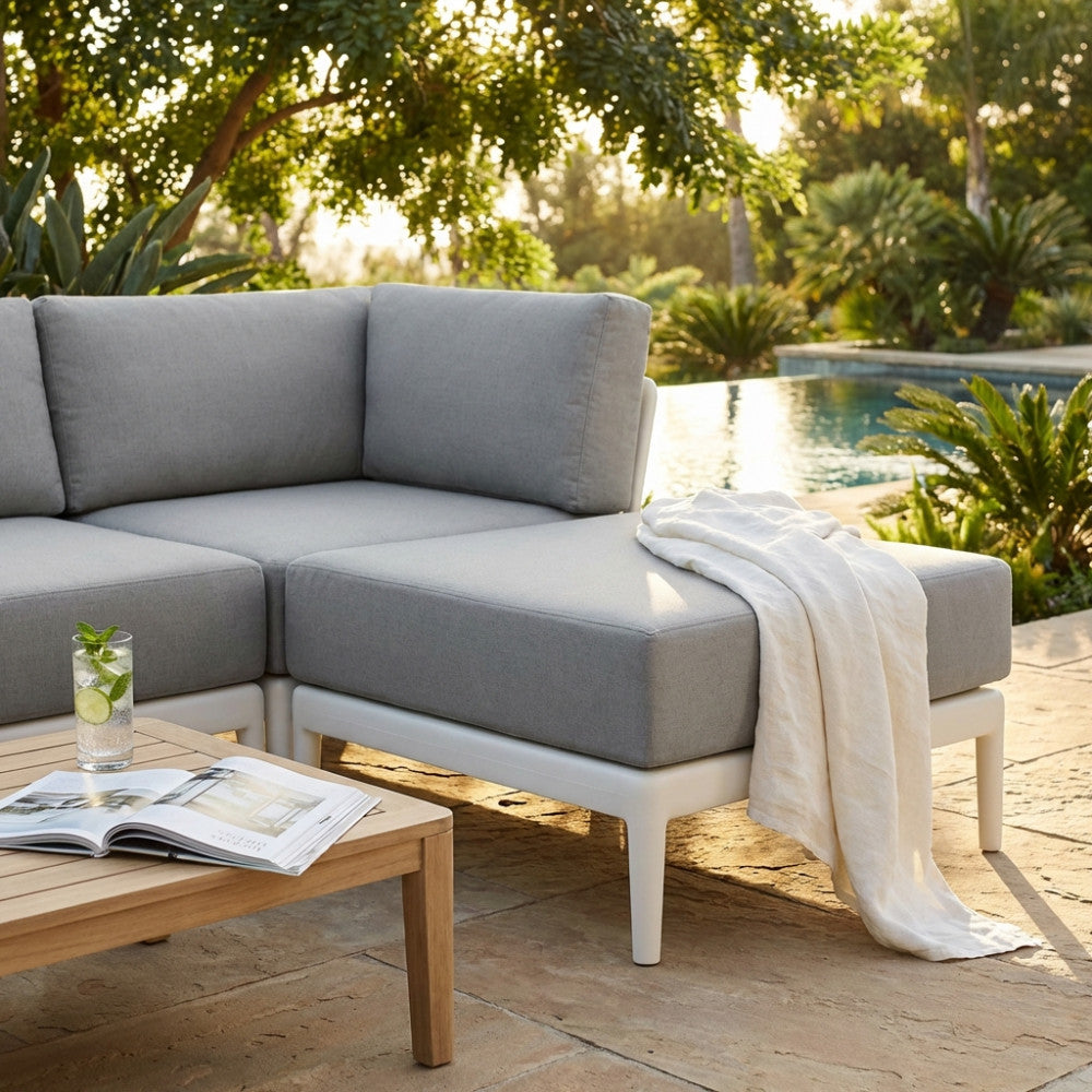 Pouf moderno Guaranà in polipropilene bianco con cuscino grigio, allestito accanto a un divano coordinato a bordo piscina.