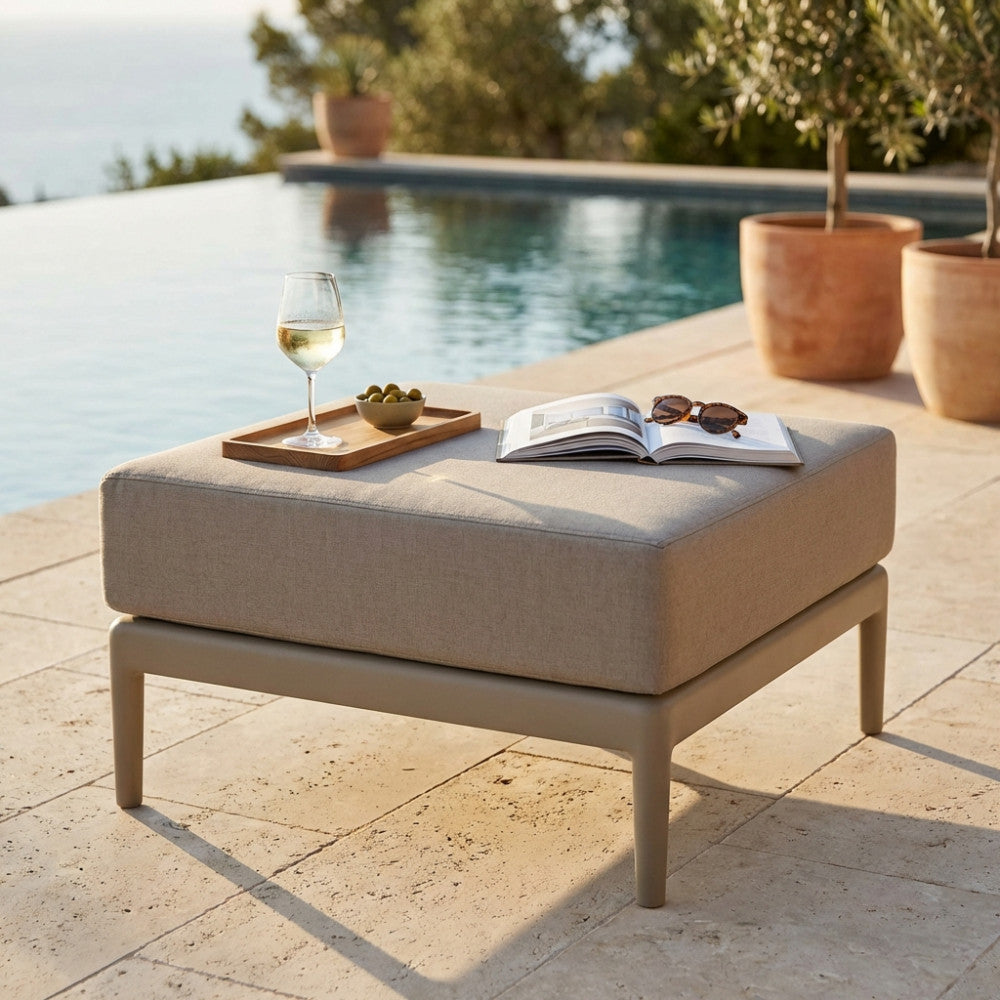 Pouf Guaranà utilizzato come piano d'appoggio elegante con vassoio in legno, calice di vino e libro aperto su una terrazza soleggiata.