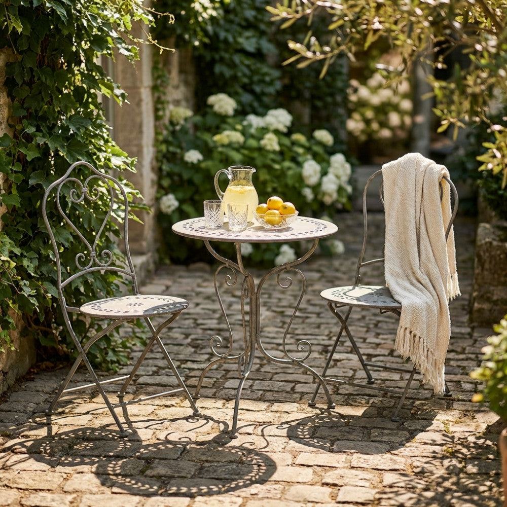 Set bistrot Jeanette in acciaio bianco ossidato ambientato in un cortile rustico con limoni e bevande fresche.