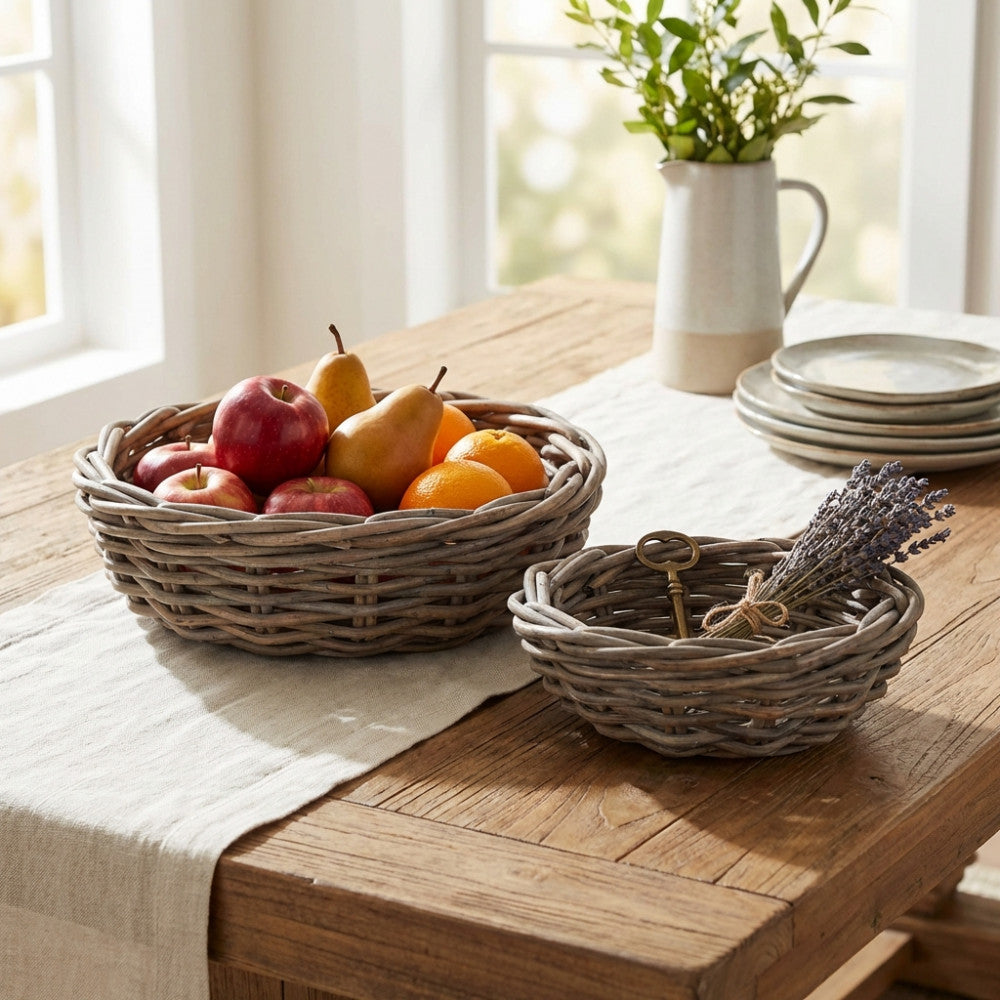 Cesti decorativi in vimini grigio disposti su un tavolo da pranzo in legno rustico, contenenti frutta di stagione e un mazzetto di lavanda essiccata.