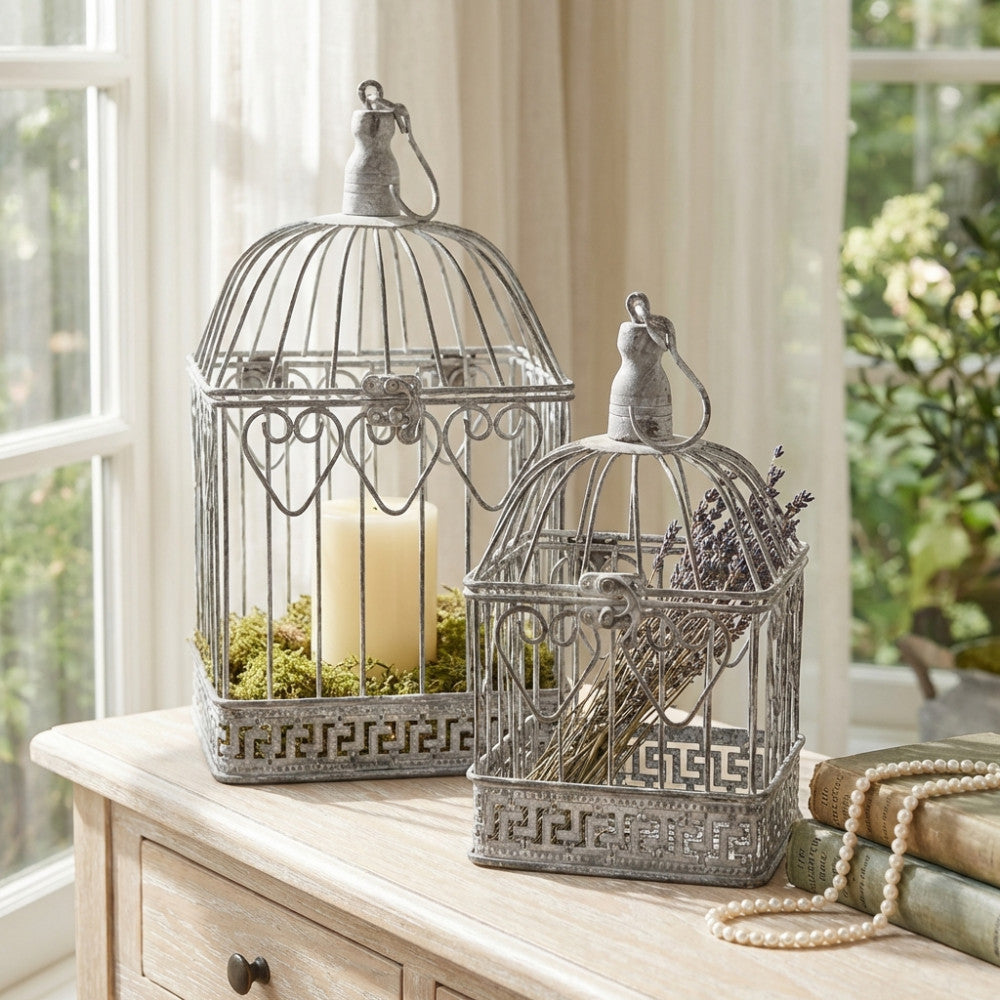 Set di due gabbie decorative in acciaio bianco ossidato, allestite con candele e lavanda su un mobile in legno chiaro.